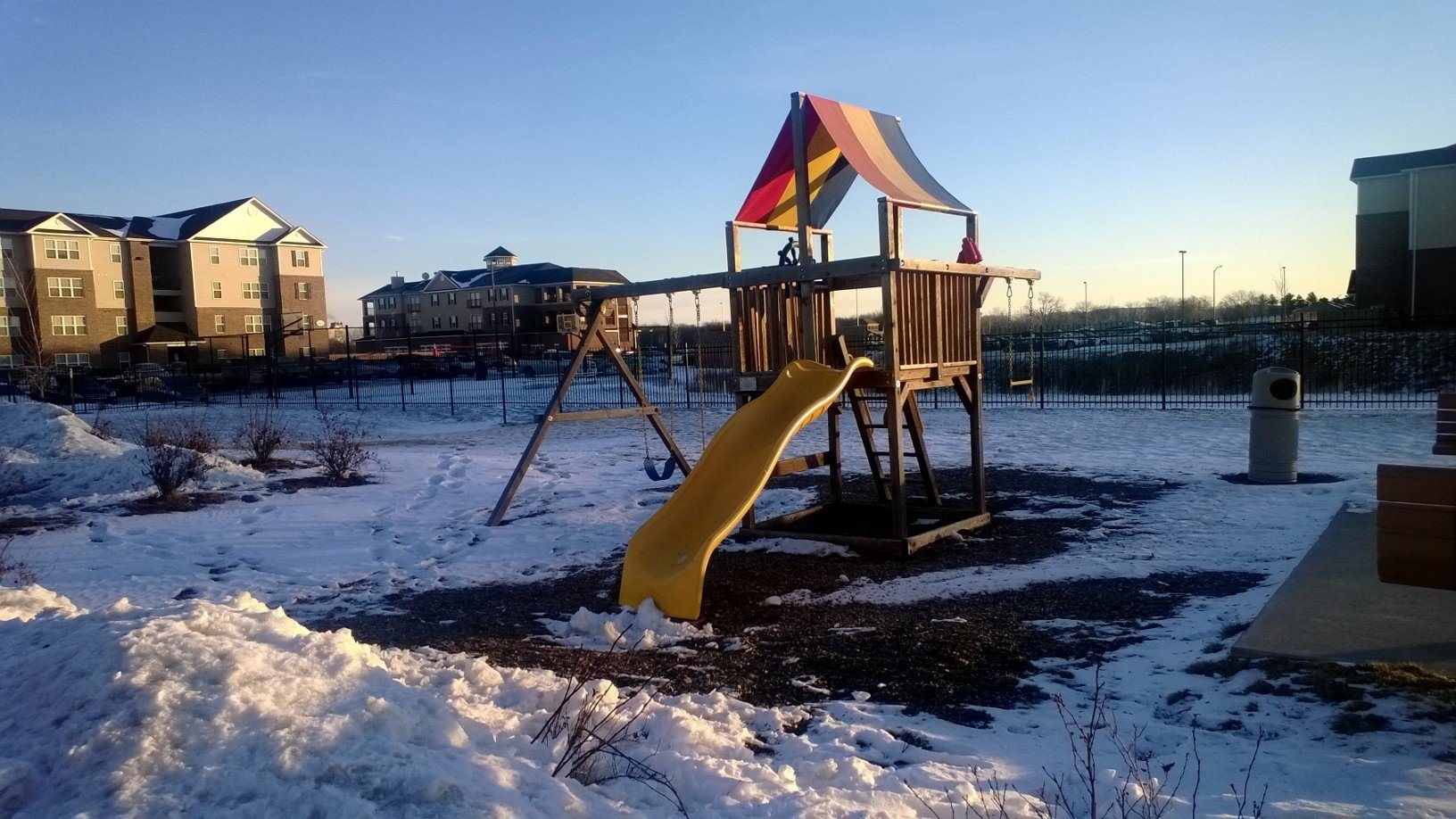 A playground with a yellow slide and a red and yellow umbrella.,A playground with a yellow slide and a red and yellow umbrella.